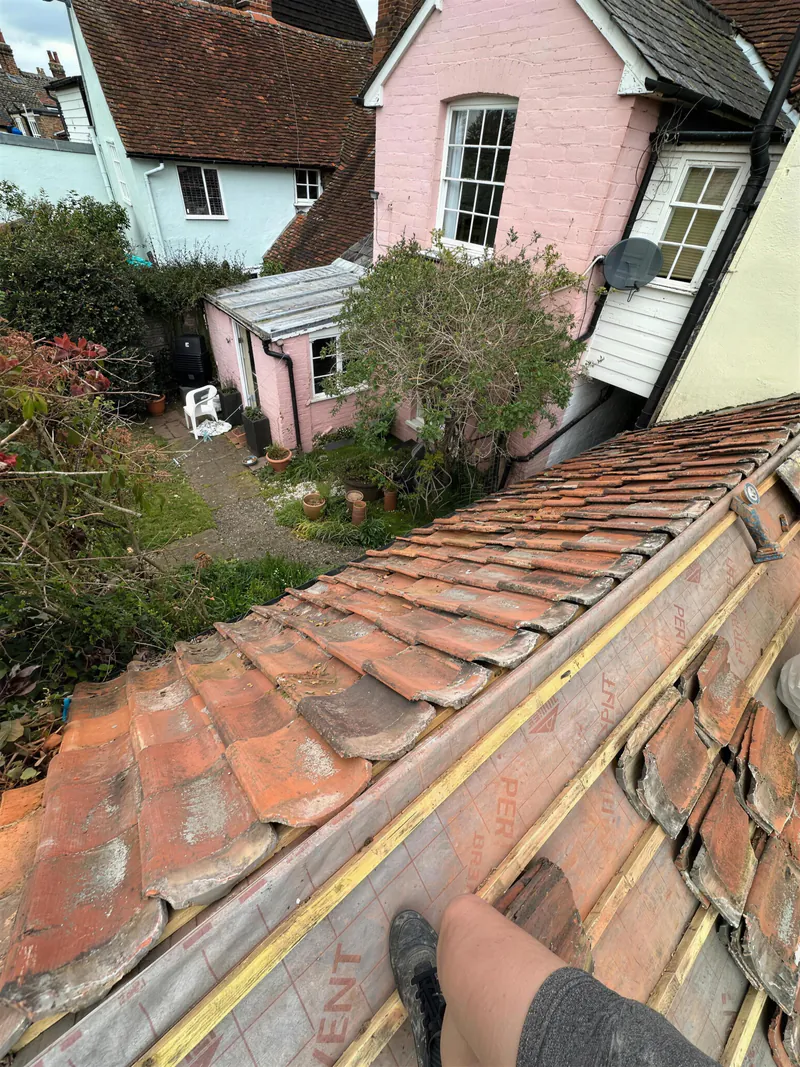 Clay pantiles being relaid on new battens behind a period cottage
